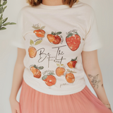 Close-up of the Be the Fruit graphic T-shirt, featuring hand-drawn fruit illustrations with faith-based words like love, kindness, and joy.