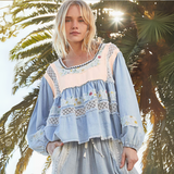 Model wearing a vintage boho patchwork blouse with lace and floral embroidery, standing in front of palm trees.