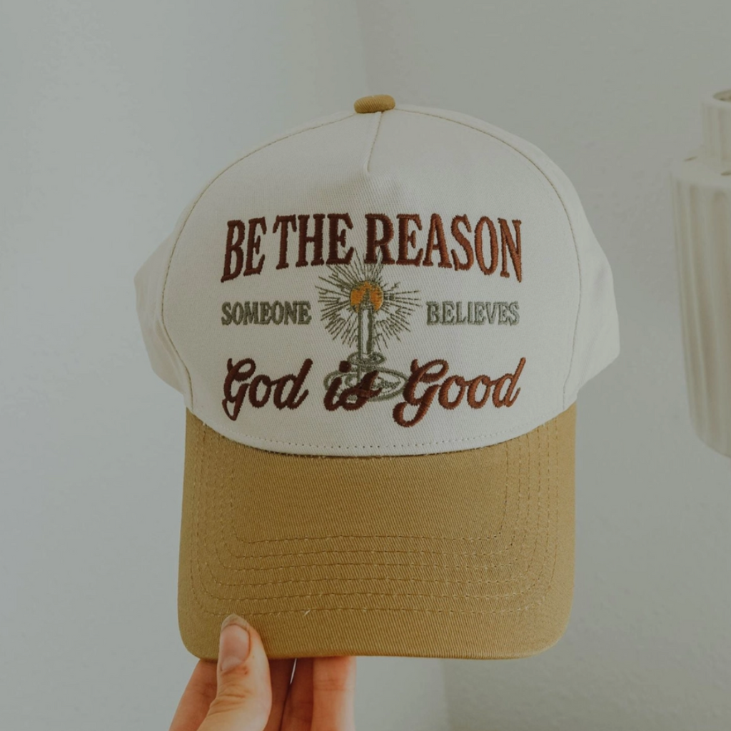Close-up of tan and cream hat with “Be the Reason Someone Believes God is Good” embroidered design.
