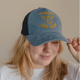 Front view of woman modeling positive message trucker hat with mesh back and curved brim.