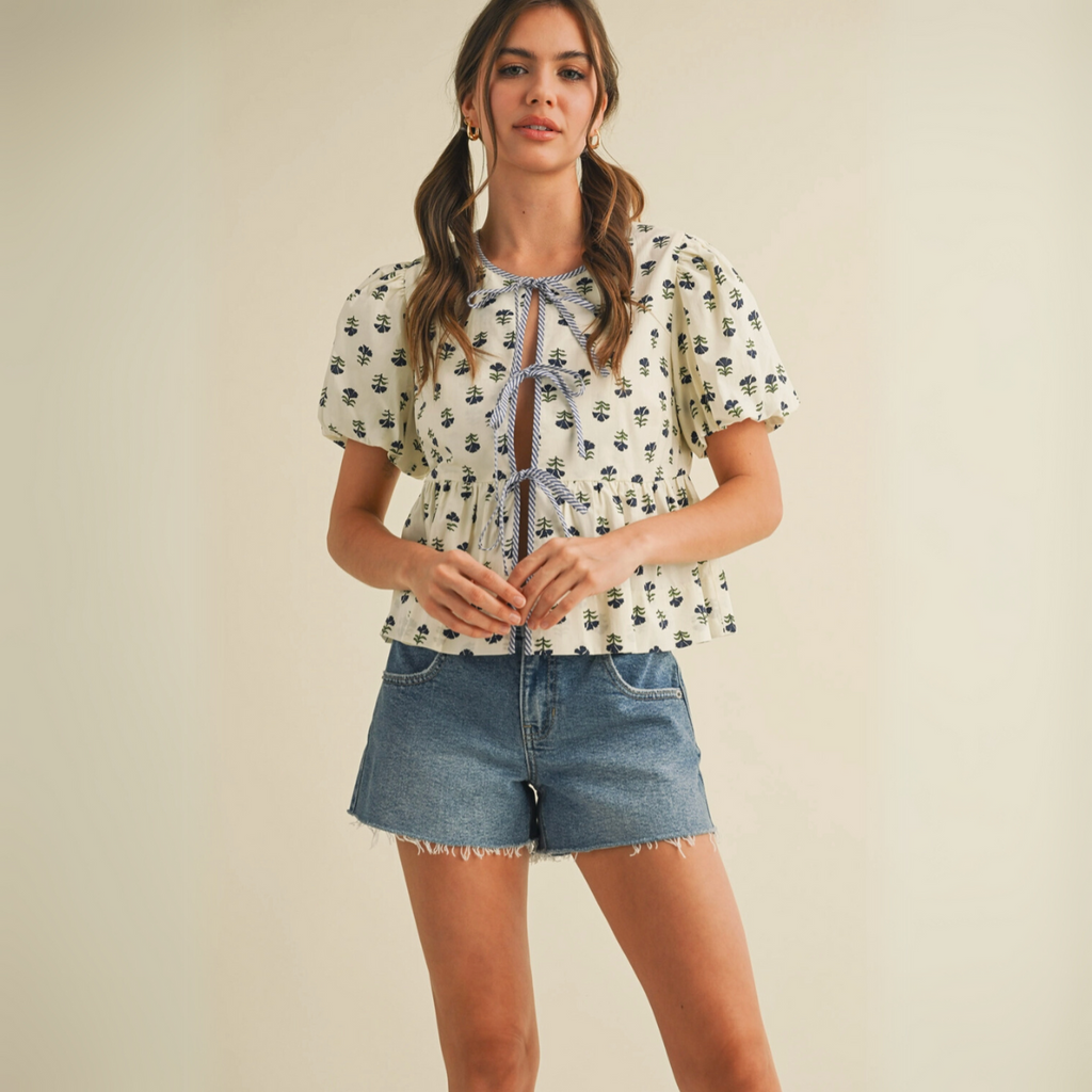 Cream peplum blouse with navy floral print and tie-front closure worn by female model in studio setting.