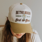 Woman wearing embroidered faith cap with tan brim and brown/green thread.