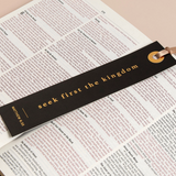 "Foil-stamped black bookmark with 'Seek first the kingdom' laying across an open Bible."