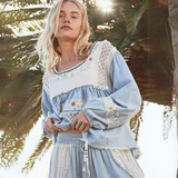 Close-up of a blue and white boho blouse featuring lace details, floral embroidery, and tiered fabric.