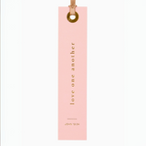 "Pink foil-pressed bookmark with scripture John 13:34 - 'Love one another' in gold lettering."