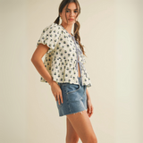 Cream peplum blouse with navy floral print and tie-front closure worn by female model in studio setting.