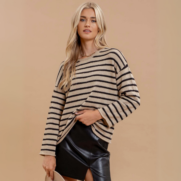 Woman wearing a boat neckline striped knit pullover sweater with long sleeves, styled with a leather skirt against a beige background.