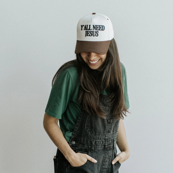 Front view of the "Y'all Need Jesus" trucker hat showcasing navy puff embroidery on the brown cap.