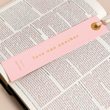 "Gold foil 'Love one another' bookmark styled across open Bible pages."