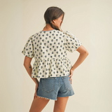 Cream peplum blouse with navy floral print and tie-front closure worn by female model in studio setting.