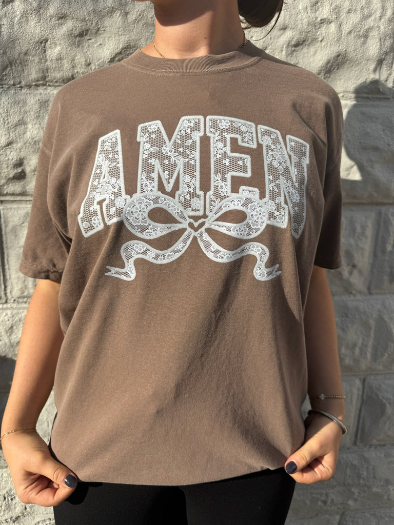 Close-up of brown "AMEN" graphic tee showcasing intricate lace pattern and bow illustration on Comfort Colors fabric.