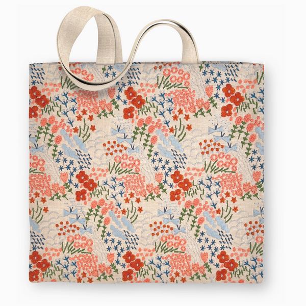 Front view of fabric tote bag featuring hand-embroidered wildflowers in coral, red, and blue with sturdy beige shoulder straps