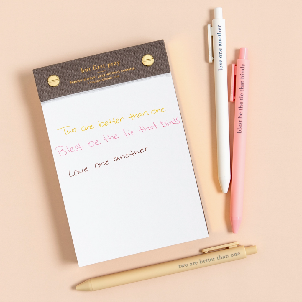 Faith-based pens writing spiritual phrases in ink, laid out on a flat-lay with a notepad.

