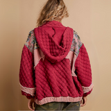 Close-up of an oversized red quilted jacket highlighting floral print and contrast patchwork design, styled over a white lace top.