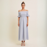 Model wearing the blue off-shoulder smocked maxi dress, standing against a neutral backdrop.