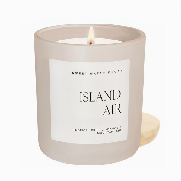 A lit Island Air candle in a white frosted glass jar with minimalist label, placed on a white background.