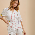 Woman wearing embroidered short-sleeve white button-up with red scallop detail and summer fruit embroidery.