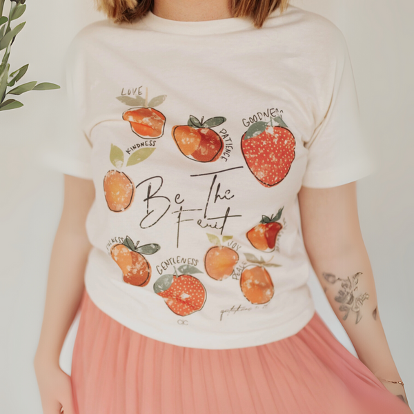 Close-up of the Be the Fruit graphic T-shirt, featuring hand-drawn fruit illustrations with faith-based words like love, kindness, and joy.
