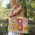 Woman holding a handmade crochet tote bag featuring colorful patchwork squares and leather straps in a natural outdoor setting.