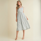 Woman wearing a blue gingham midi dress with tie straps and embroidered neckline

