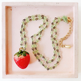 Close-up view of the Kids' Strawberry Charm Necklace featuring a red strawberry pendant and light green beads.

