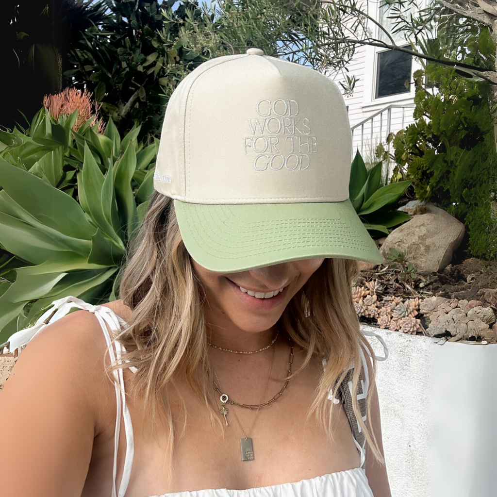 Woman wearing the 'God Works for the Good' faith-inspired trucker hat with a relaxed, casual outfit."
