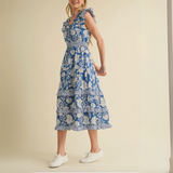 Side view of woman wearing a blue floral tiered midi dress with ruffle sleeves.

