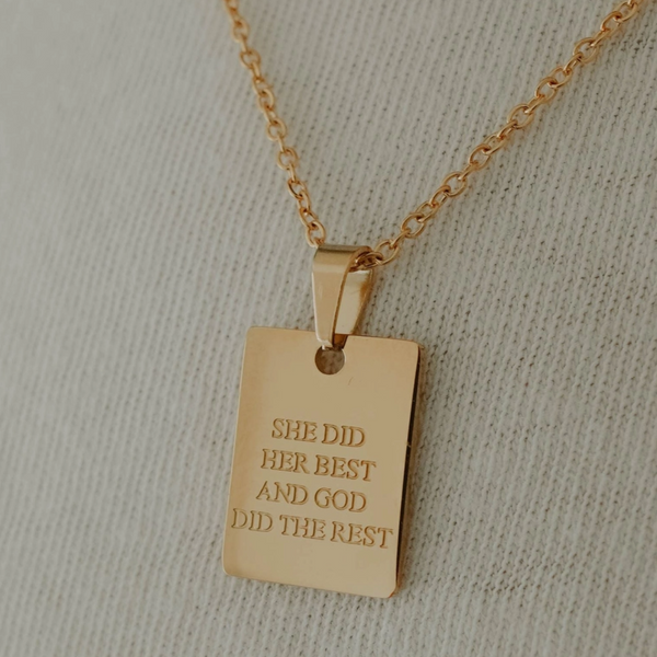 Gold necklace with “She did her best” engraved pendant on fabric.

