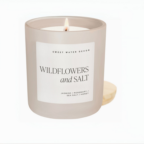 Hand holding a lit Wildflowers and Salt candle in a soft beige frosted jar with a minimalist white label.