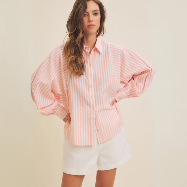 Woman wearing a pink striped button-up blouse with balloon sleeves, styled with white shorts.