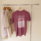 Mauve-colored ‘By His Wounds We Are Healed’ graphic T-shirt hanging on a clothing rack