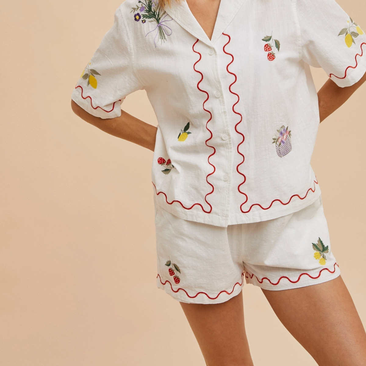 Model wearing white embroidered shorts with scallop hem and fruit designs

