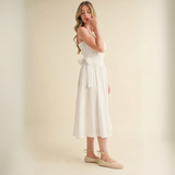 Side view of model wearing white midi dress with side tie and woven espadrille flats.

