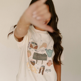 Model wearing the Outer Banks Graphic Tee, making a shaka hand gesture, showcasing the Pogue Life design and OBX-themed graphics.