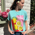 Person wearing a light blue t-shirt with a lemon design outdoors.