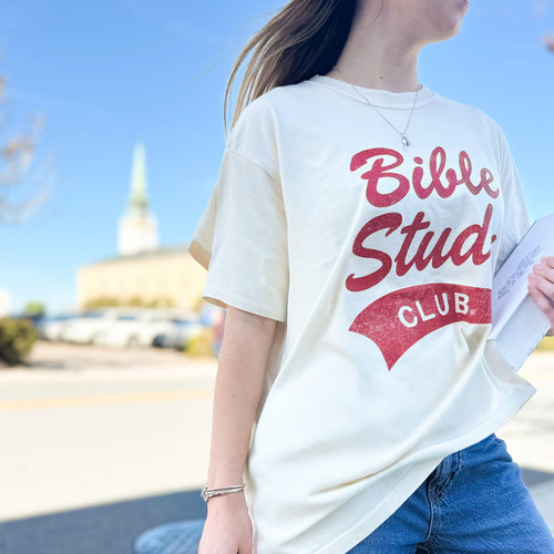 Young woman outdoors wearing a white t-shirt with 'Bible Study Club' text in red.