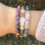 Stack of gemstone beaded bracelets on a wrist, including the White Agate Cross Bracelet, styled with other natural stone jewelry.

