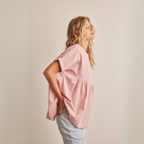 Side profile of blush pink peplum top highlighting relaxed fit and rolled sleeves.
