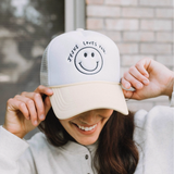 Close-up of white and beige trucker hat with smiley face and “Jesus Loves You” embroidery.

