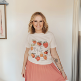 Smiling woman wearing the Be the Fruit graphic tee, styled with a flowy pink skirt for a casual and inspirational outfit.