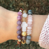 Woman wearing a stack of beaded bracelets, including the rose quartz and labradorite Agape Divine Love Bracelet.

