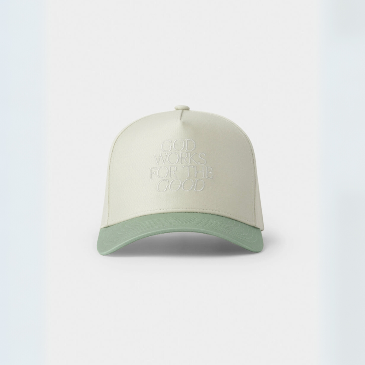 "Cream and sage green trucker hat with 'God Works for the Good' embroidered on the front panel."

