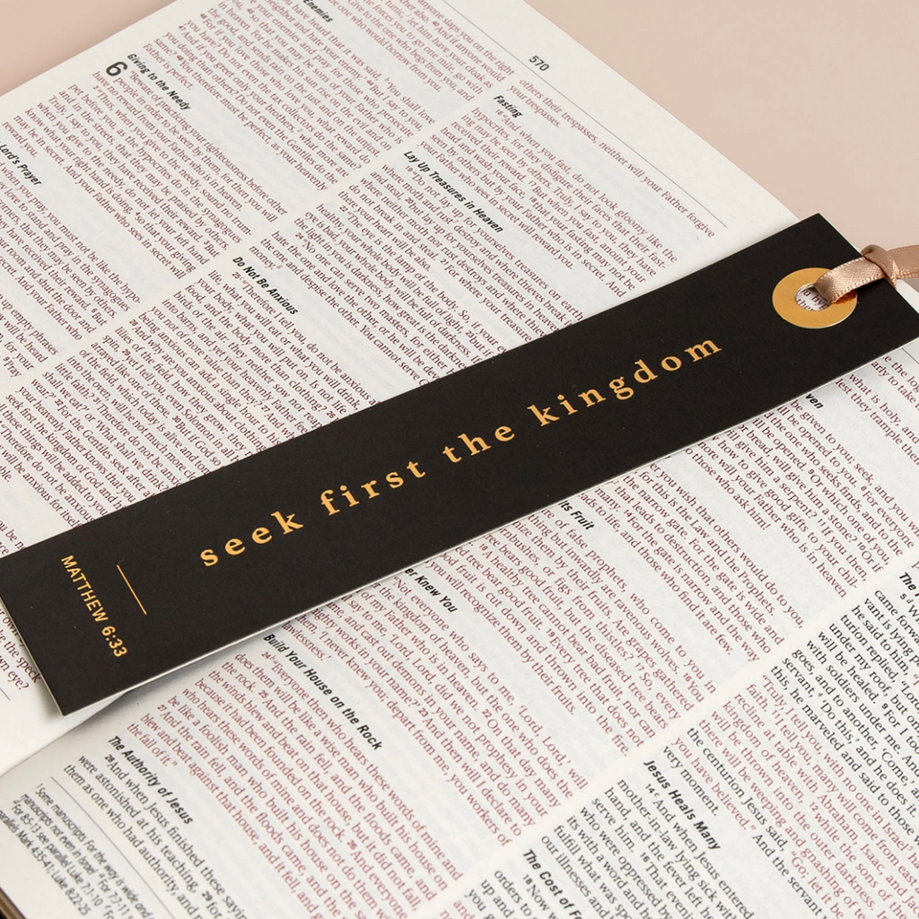 "Foil-stamped black bookmark with 'Seek first the kingdom' laying across an open Bible."

