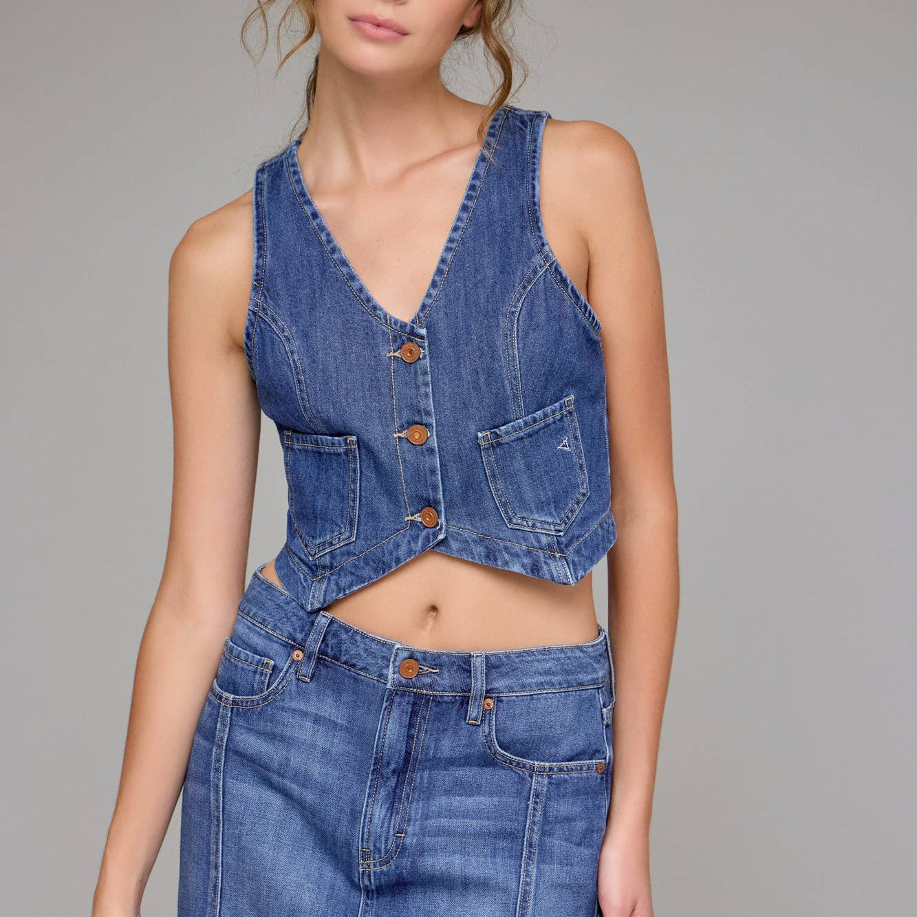 Woman wearing a denim vest and skirt set on a gray background