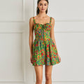 Woman wearing a colorful floral dress against a white wall.