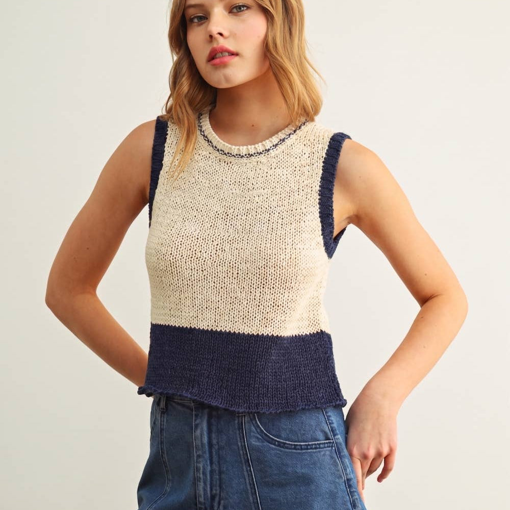 Woman wearing a two-tone sleeveless top and denim shorts on a plain background
