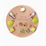 Mini Momo Tennis Earring Set featuring gold, green, and enamel tennis-themed studs displayed on a tan round leather card.