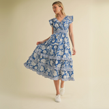 Woman twirling in blue ruffle floral dress with tiered layers and sneakers.

