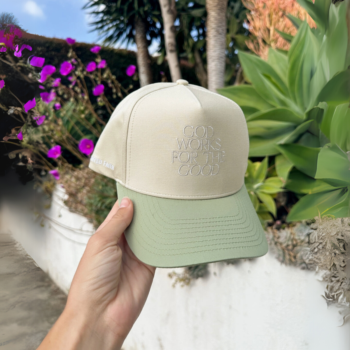 "Hand holding a faith-based trucker hat featuring sage green and cream tones with an inspirational embroidered message."

