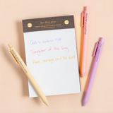 Faith-based pens writing spiritual phrases in ink, laid out on a flat-lay with a notepad.

